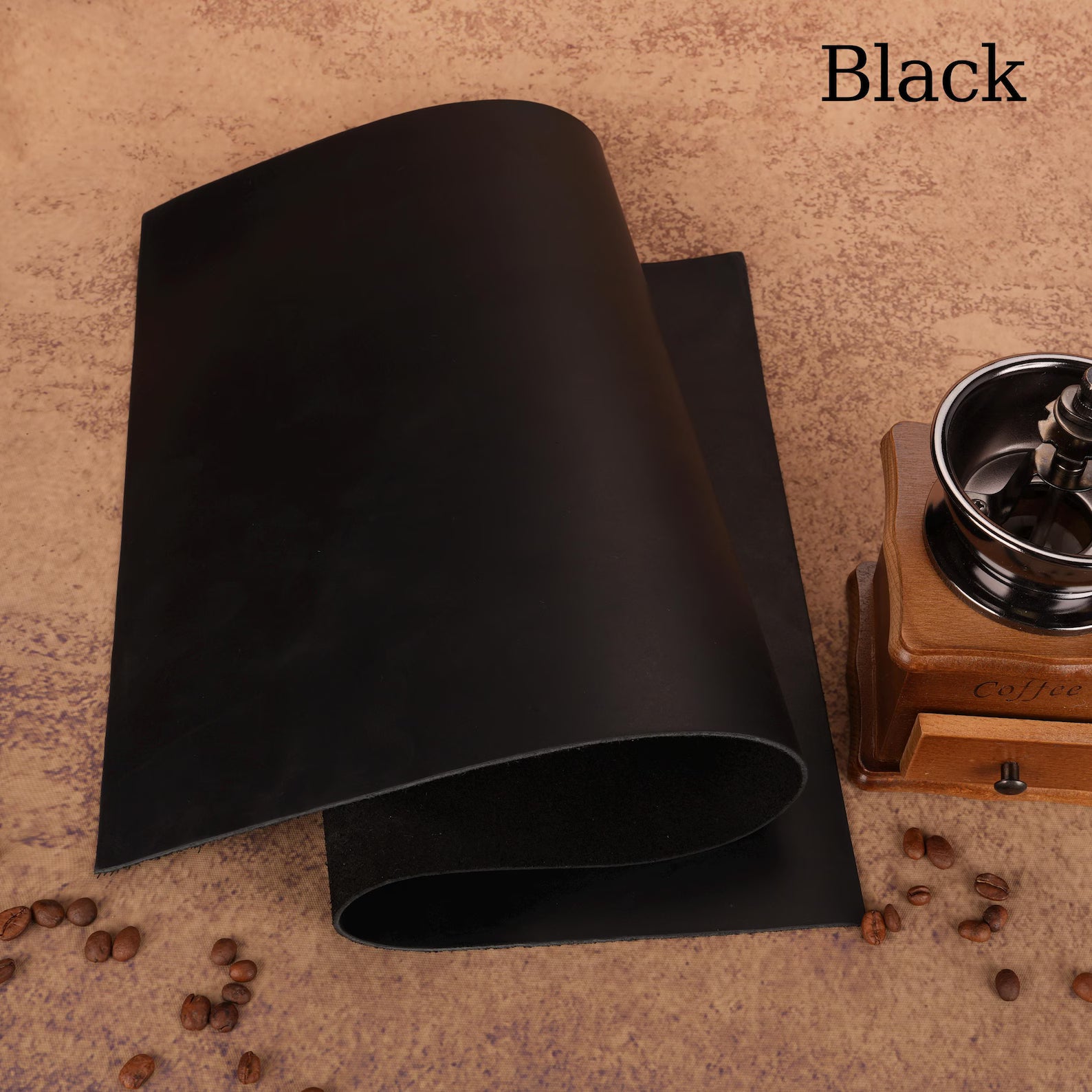 Black mat on a textured surface with coffee beans and a wooden coffee grinder.