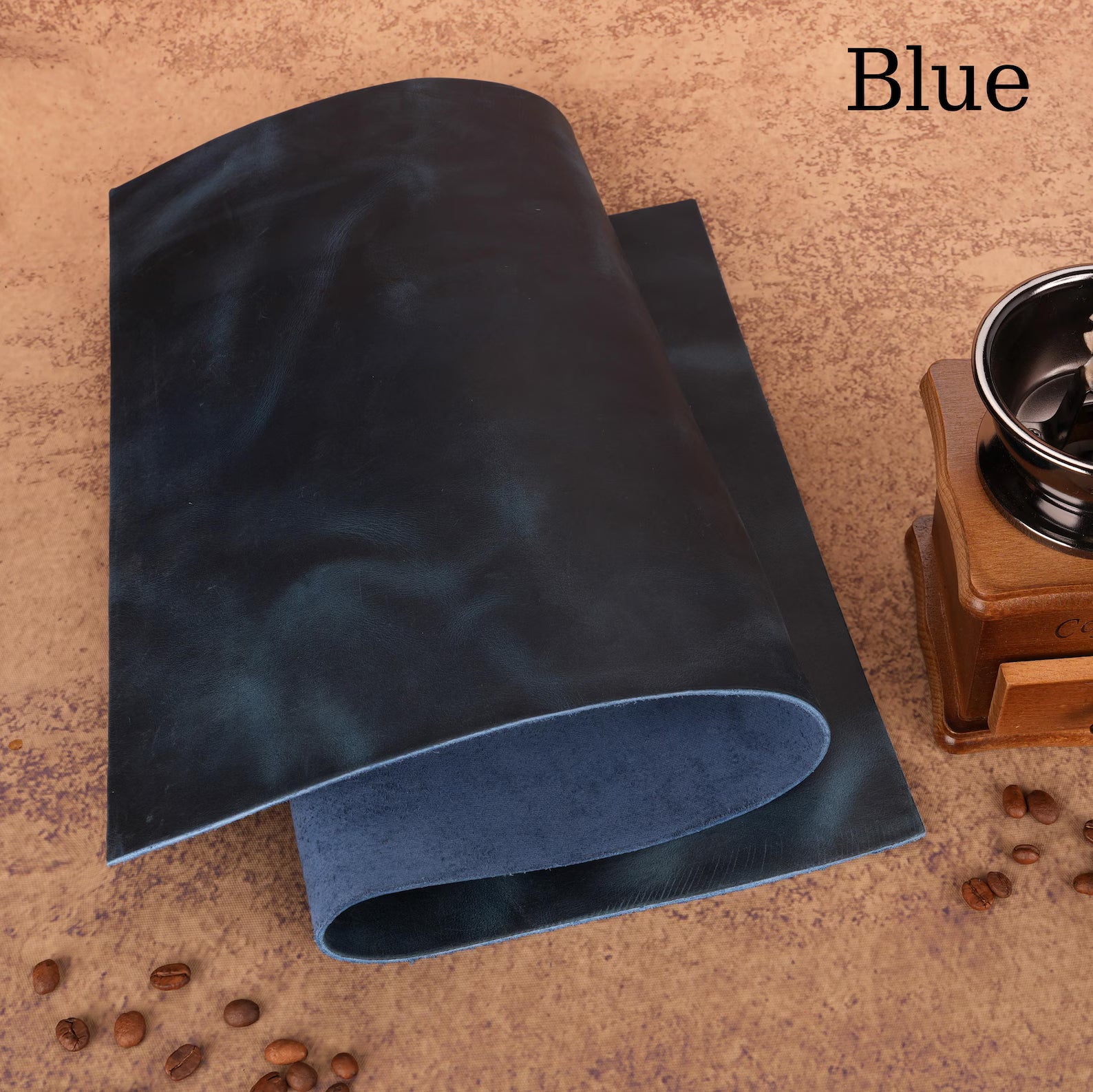 Blue leather sample on a textured surface with coffee beans and a grinder.