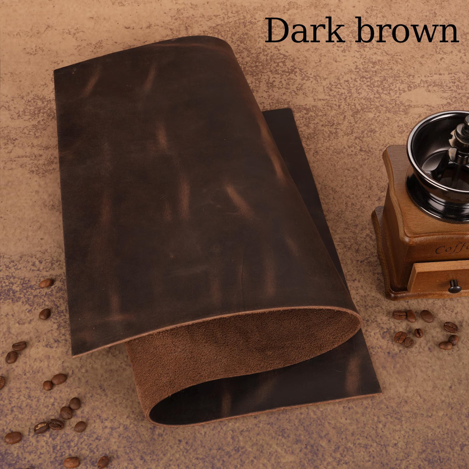 Dark brown leather sample with coffee beans and a grinder on a textured surface