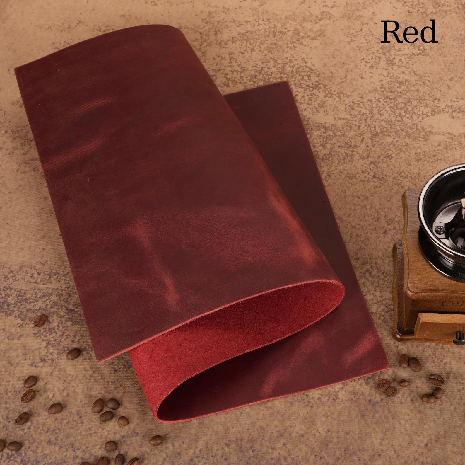 Red leather mat on a textured surface with coffee beans and a coffee grinder.